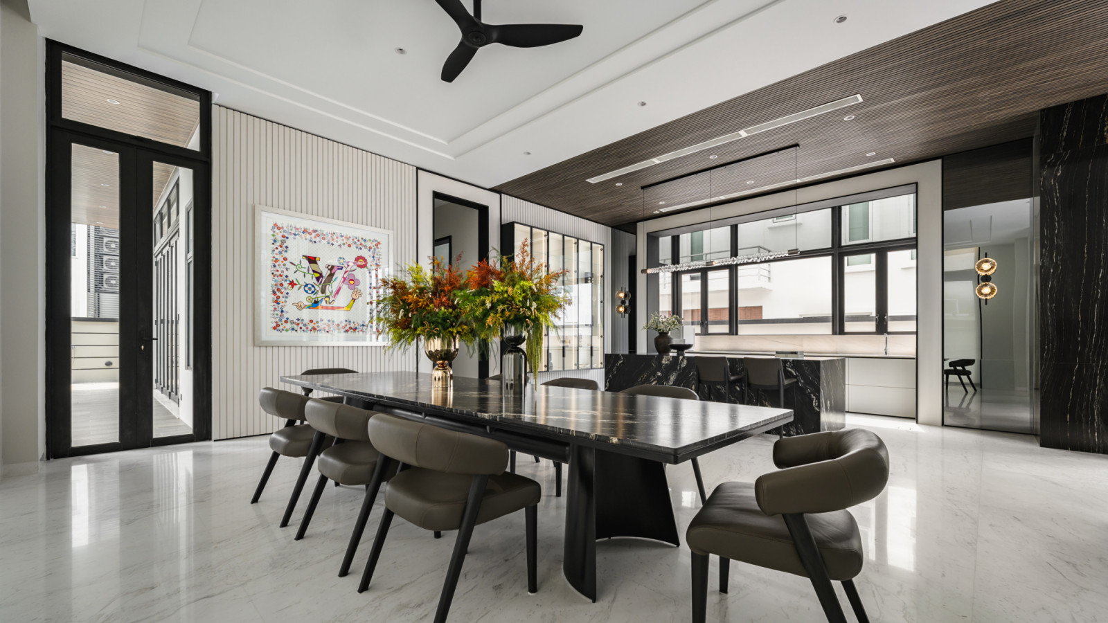 The dining area features a dramatic black marble table that serves as both functional furniture and sculptural element, with soaring ceilings that showcase the home’s remarkable natural light quality