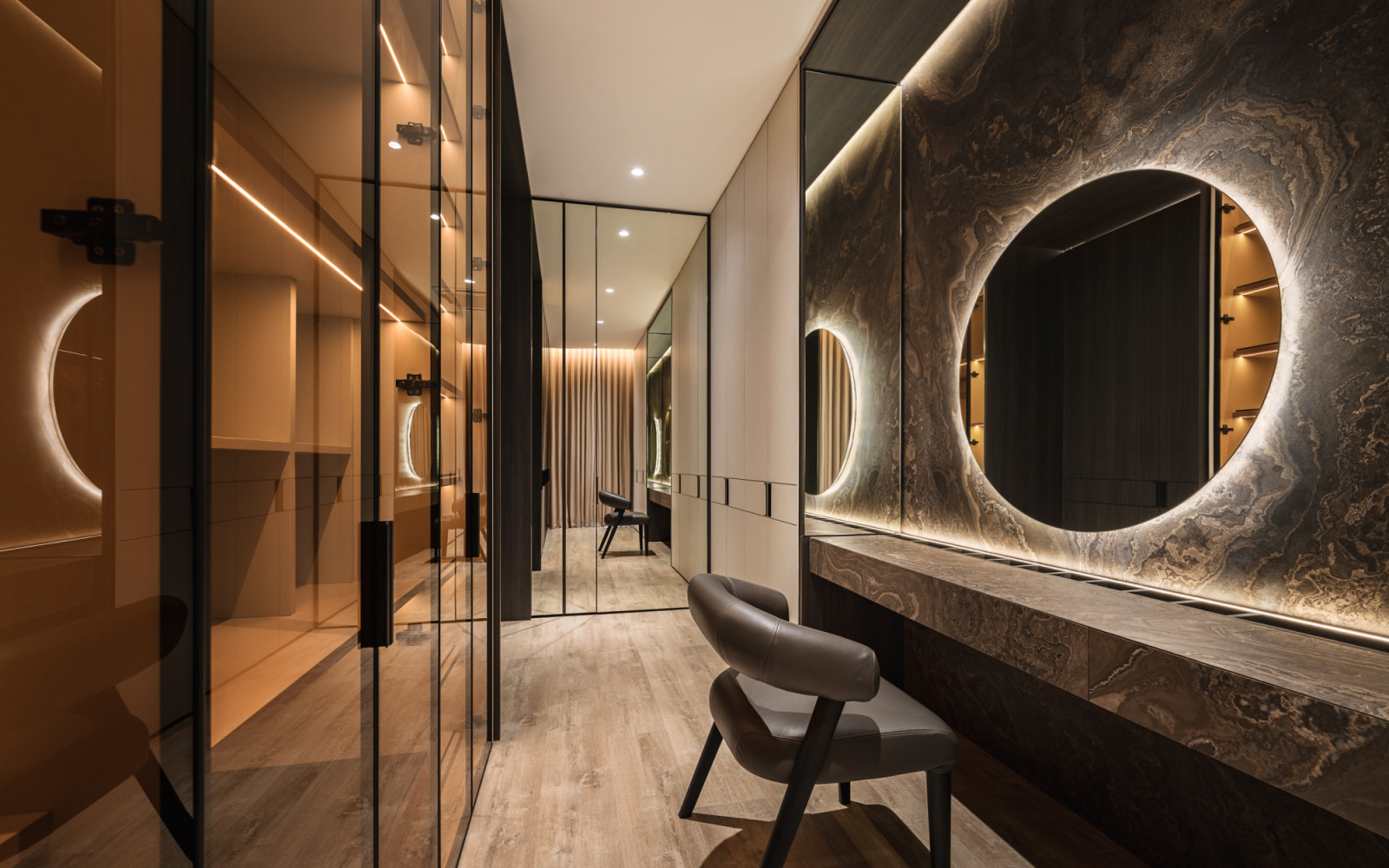 The walk-in closet’s “soft glow of backlit mirrors” and curved seating elements create an intimate dressing area