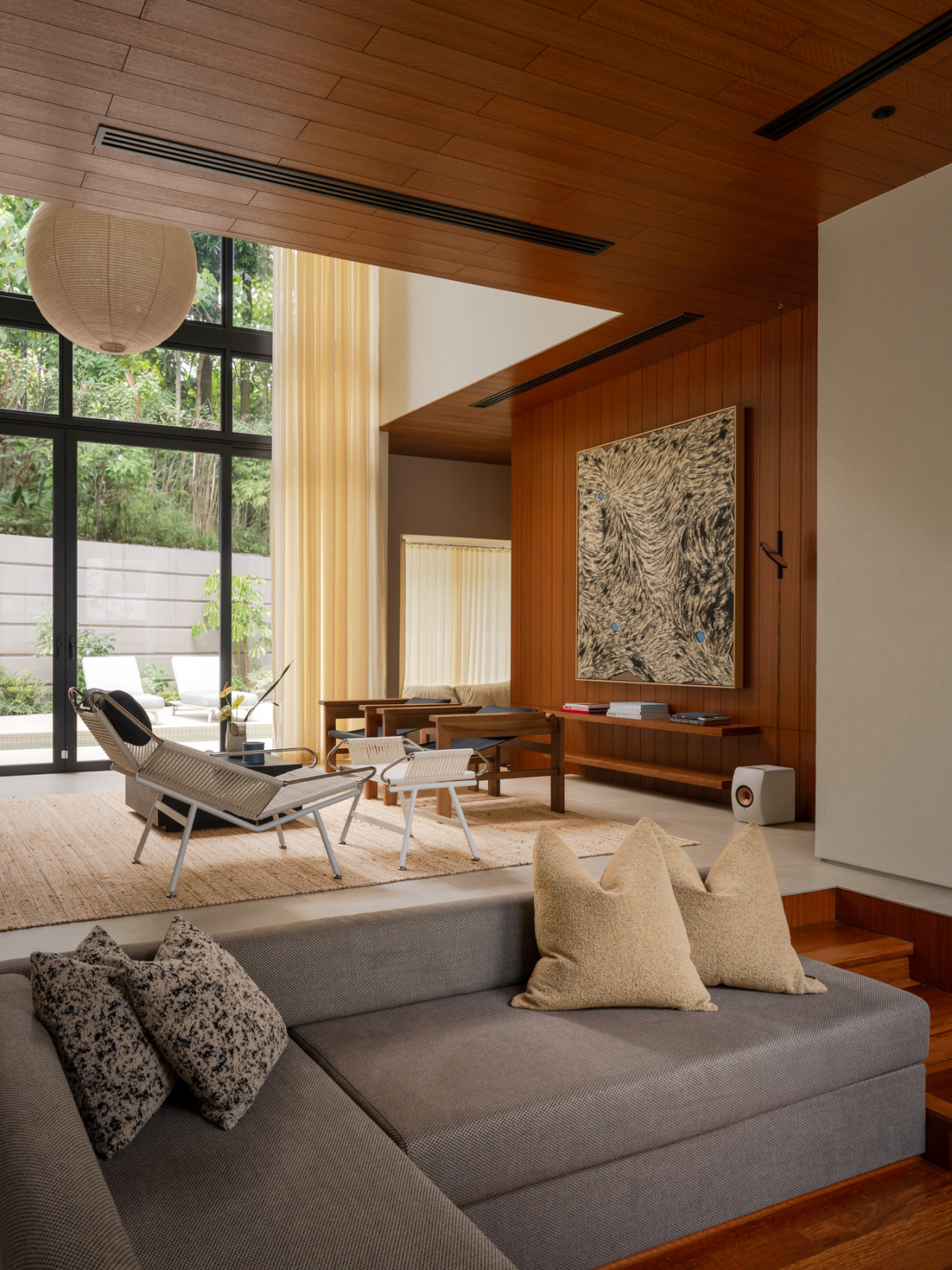 The sunken conversation pit, inspired by the 1970s Monica and Simon Siegel House designed by David Shelley leads to the double-volume living area clad in rich veneered planks and featuring a distinctive artwork by Nazhan Fikri