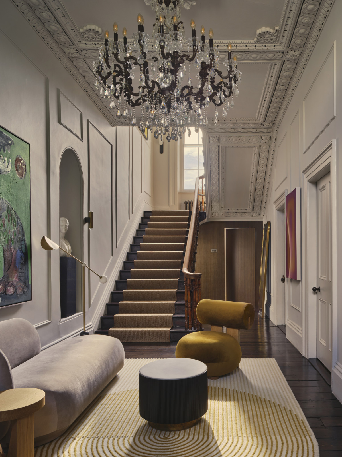 The entryway to a Dublin, Ireland home designed by Maison RA-D, featuring a Hippo Lounge Chair by NOR11, chaise lounge by Ferm Living, Nori Coffee Table by Gallotti Radice, Ply Rug by GAN, Balance Floor Lamp by Square in Circle, Plinth Pedestal by Audo CPH, Diana Cacciatrice, Galleria Romanelli (white-bust) by Artemest, vector light wall sconce by Square in Circle, Mundy Veneer Wall with a concealed door by DFL, and Cugino Side table by Gubi