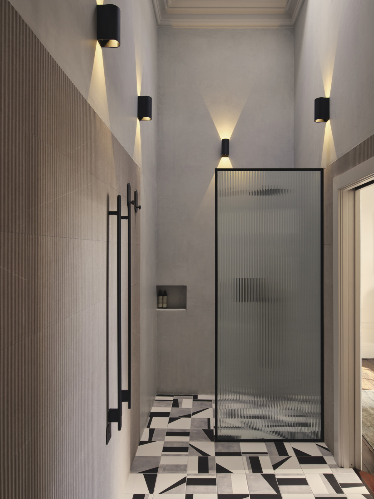 The primary bathroom in a Dublin, Ireland home designed by Maison RA-D, with a Rigo Towel Warmer by Antonio Lupi, Collect Hook Space Copenhagen by AndTradition, microcement wall, tiling in Play Edge Mix by ABK, shower and tap fittings by Gattoni, and bespoke joinery by DFL