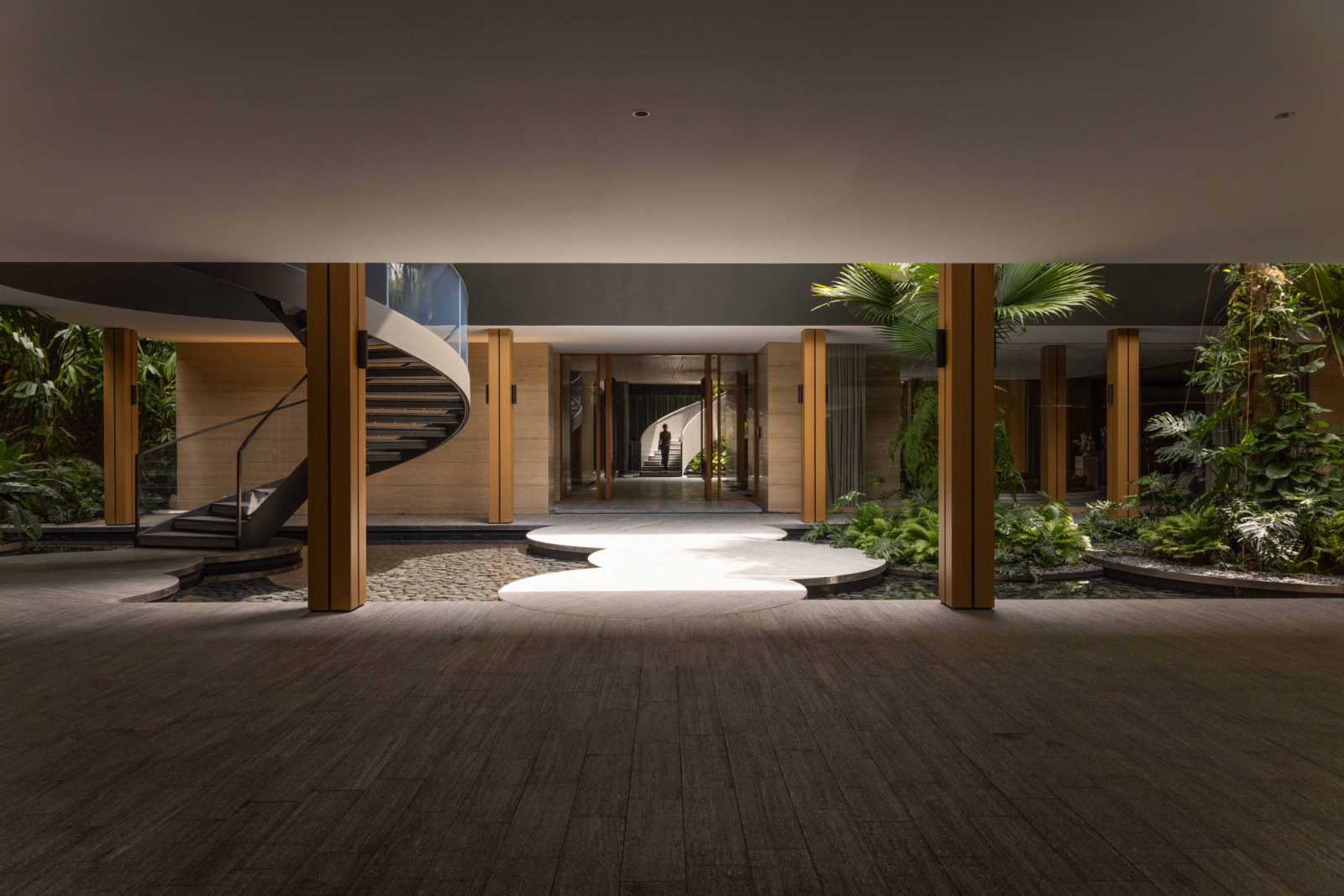 A sequence of circular stepping stones leads across the courtyard to a sculptural spiral staircase, embodying the house’s play of compression and release, shadow and light