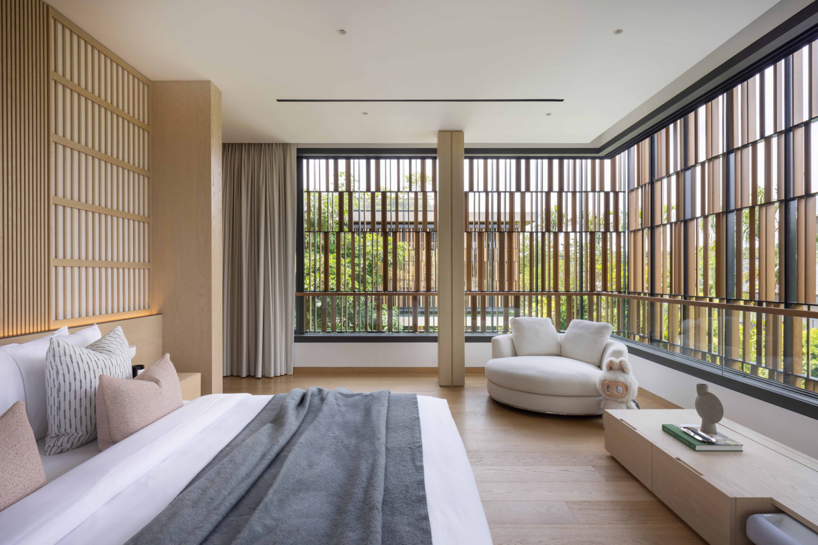 This corner bedroom features a screened view of the greenery outside, with a Labubu figure adding personality to its neutral palette