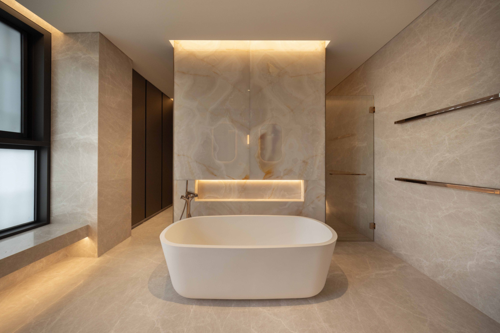 This marble-clad bathroom features a softly lit wall niche
