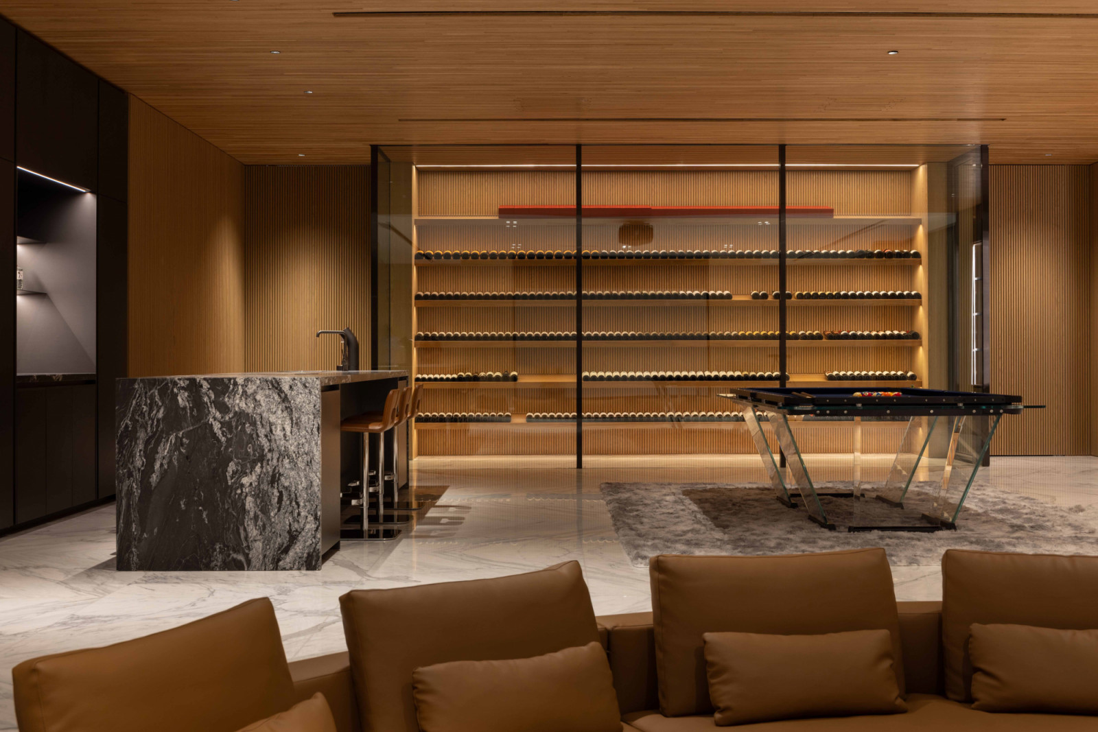 One corner of the basement features a marble-clad bar, a glass-base pool table, and a glazed, climate-controlled wine cellar