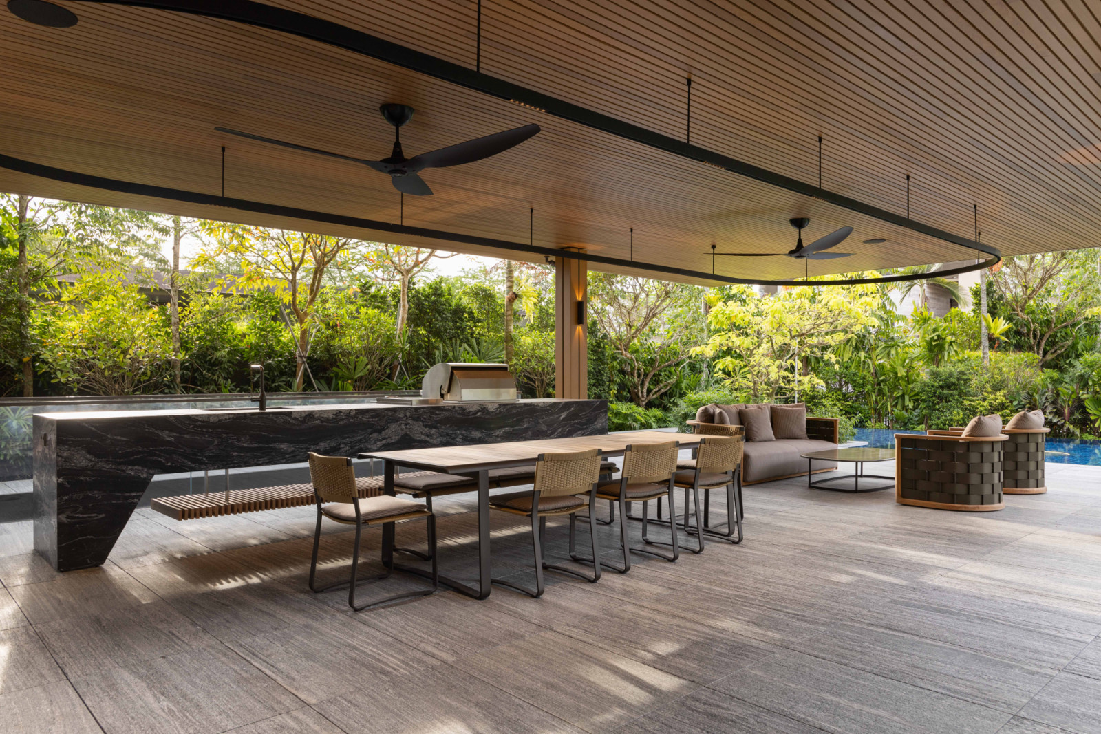 This expansive outdoor area features a marble bar counter, woven dining set and plush lounge seating, opening to the greenery and poolside views