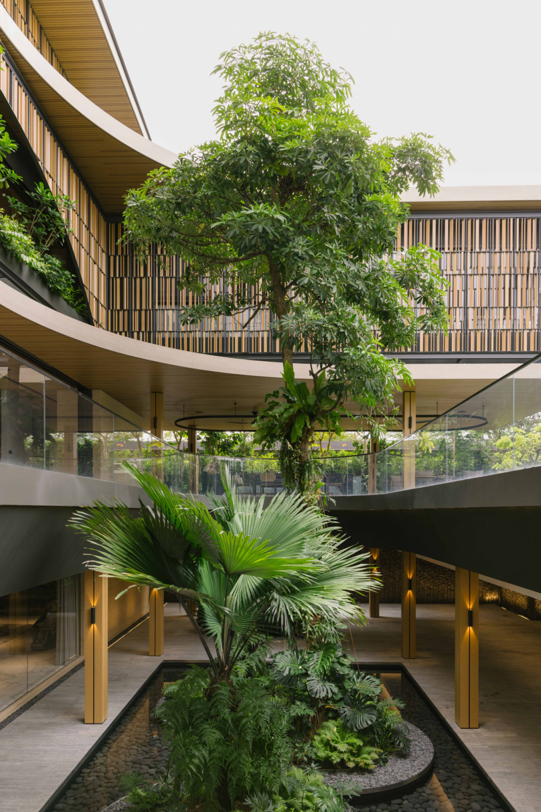 A courtyard carved into the basement draws daylight and breezes deep into the home, while tall trees, shrubbery and water add a lush, tropical vitality