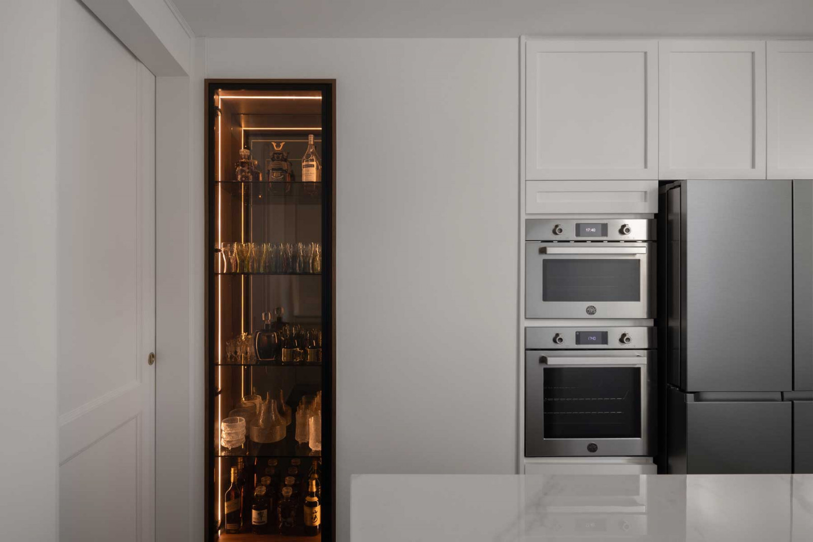 A warm-toned glass display cabinet adds contrast to the monochromatic kitchen