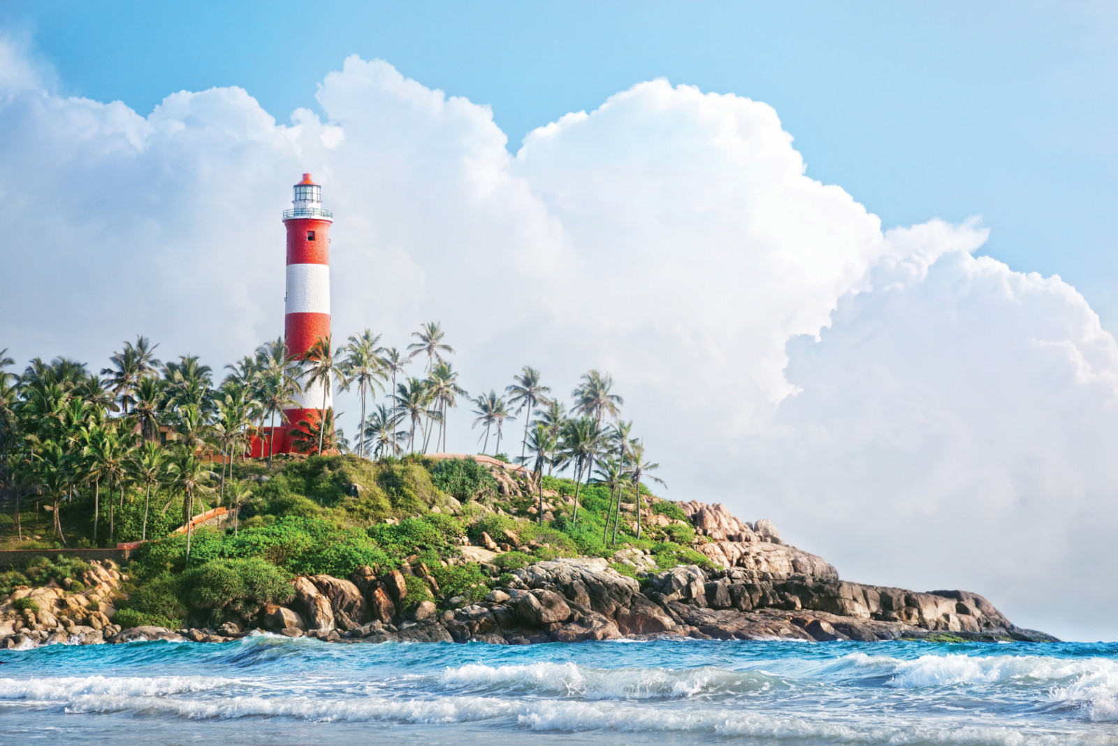 Lighthouse on the rocks near the ocean at blue sky with big white clouds in Kovalam, Kerala, India
