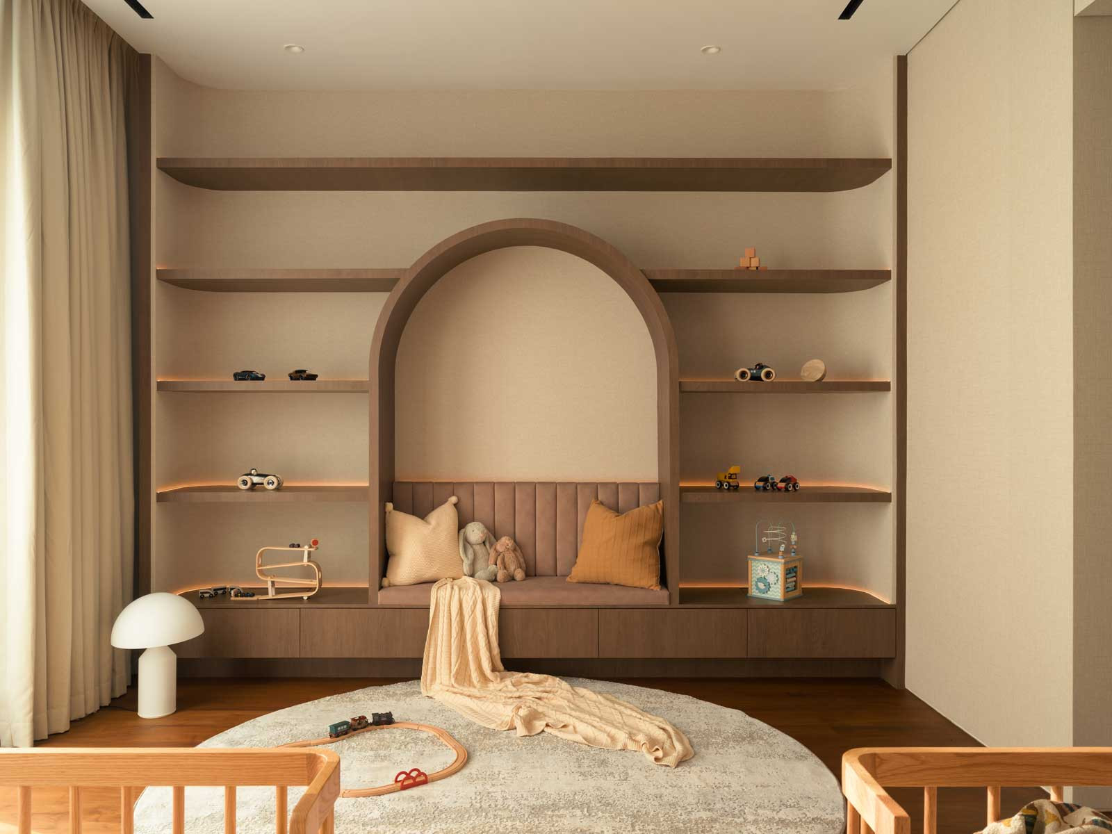 A display wall with curved carpentry anchored by an arched seating nook brings a dreamy touch to the children’s bedroom