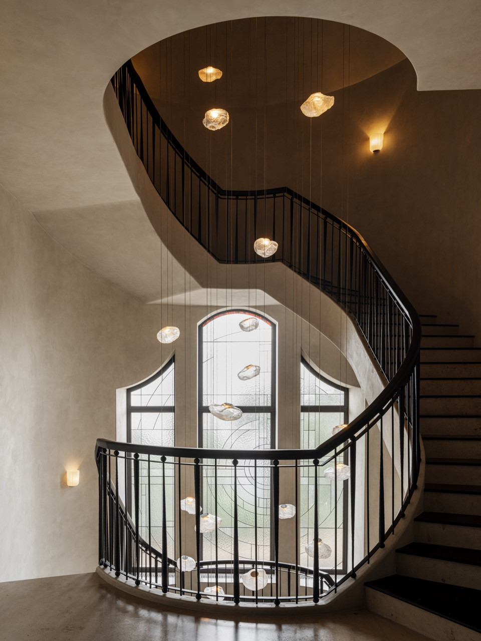 Staircase landing with arched stained-glass window, Bocci pendant lights, and metal railings overlooking the entrance hall below