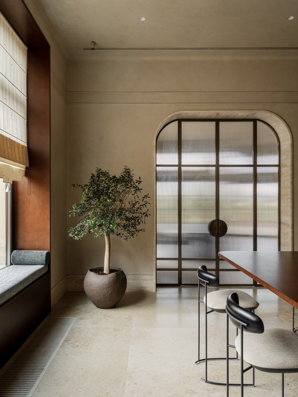 Kitchen-dining view highlighting arched glass doors with a brass frame, a custom dining table, and book-matched marble visible in the adjacent kitchen area