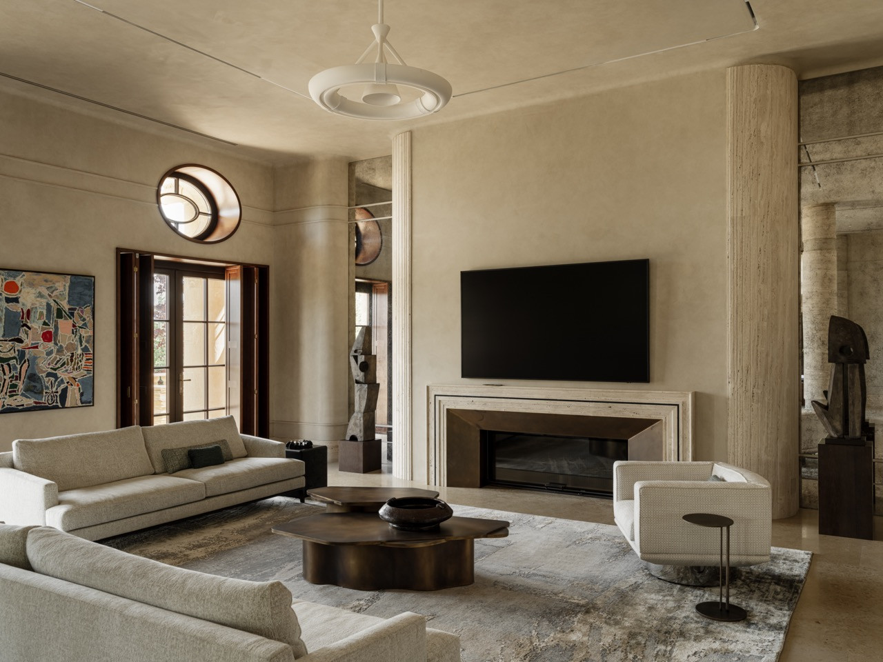 Living room from an alternate angle showing the connection to outdoor spaces through dark wood-framed French doors and the circular Art Deco-inspired ceiling lights are visible, along with the Nadya Bloch painting and travertine columns