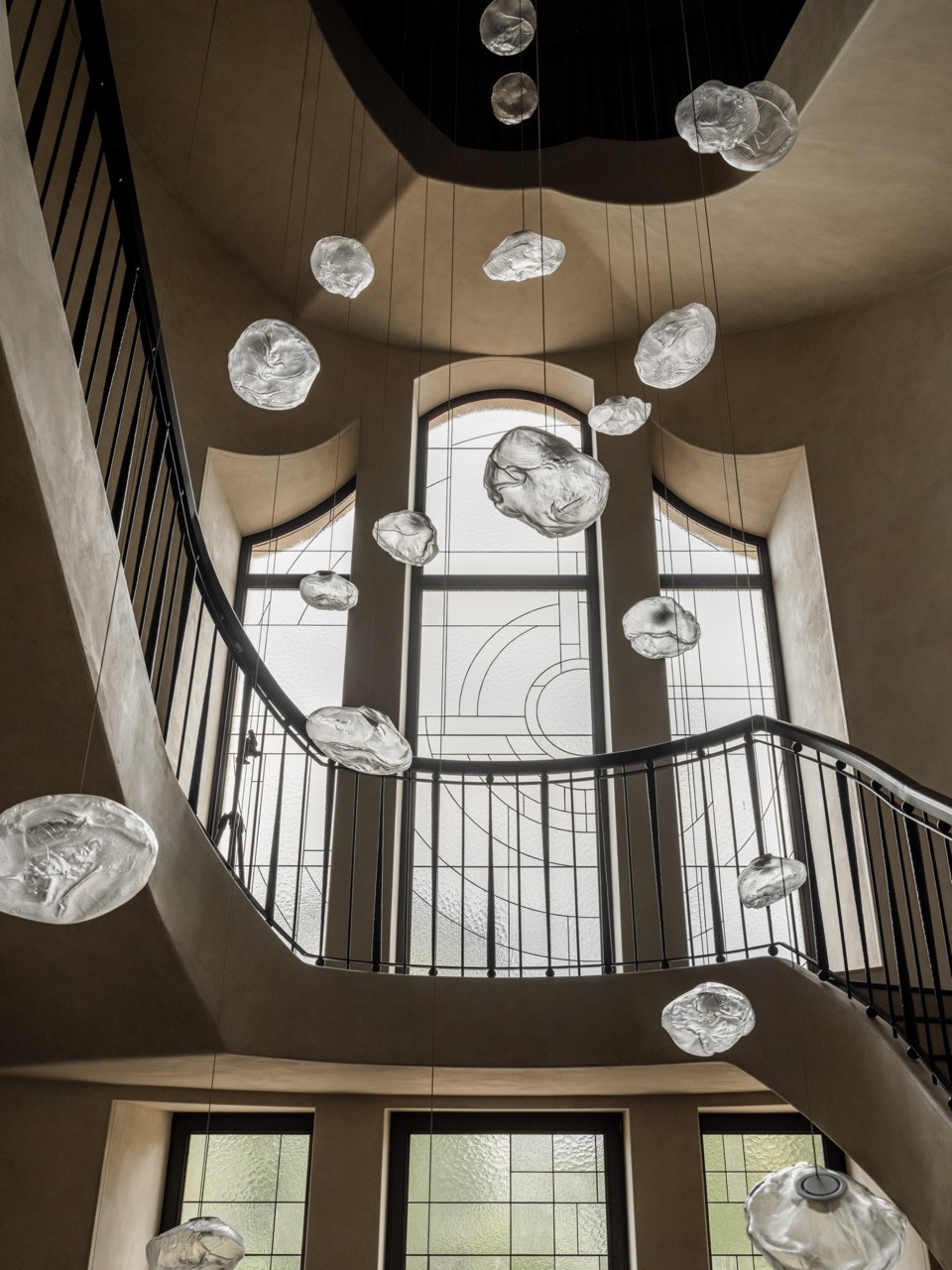Upward view in staircase hall showing curved metal railings, Nero Marquina marble steps, and multiple Bocci glass pendants suspended at varying heights