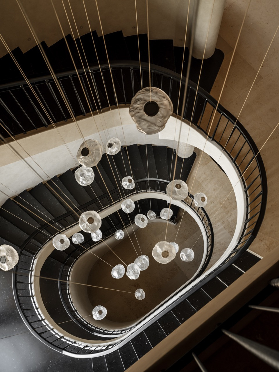 Aerial view of the staircase hall showing Nero Marquina marble steps, curved metal railings, and Bocci hand-blown glass pendants descending through the space