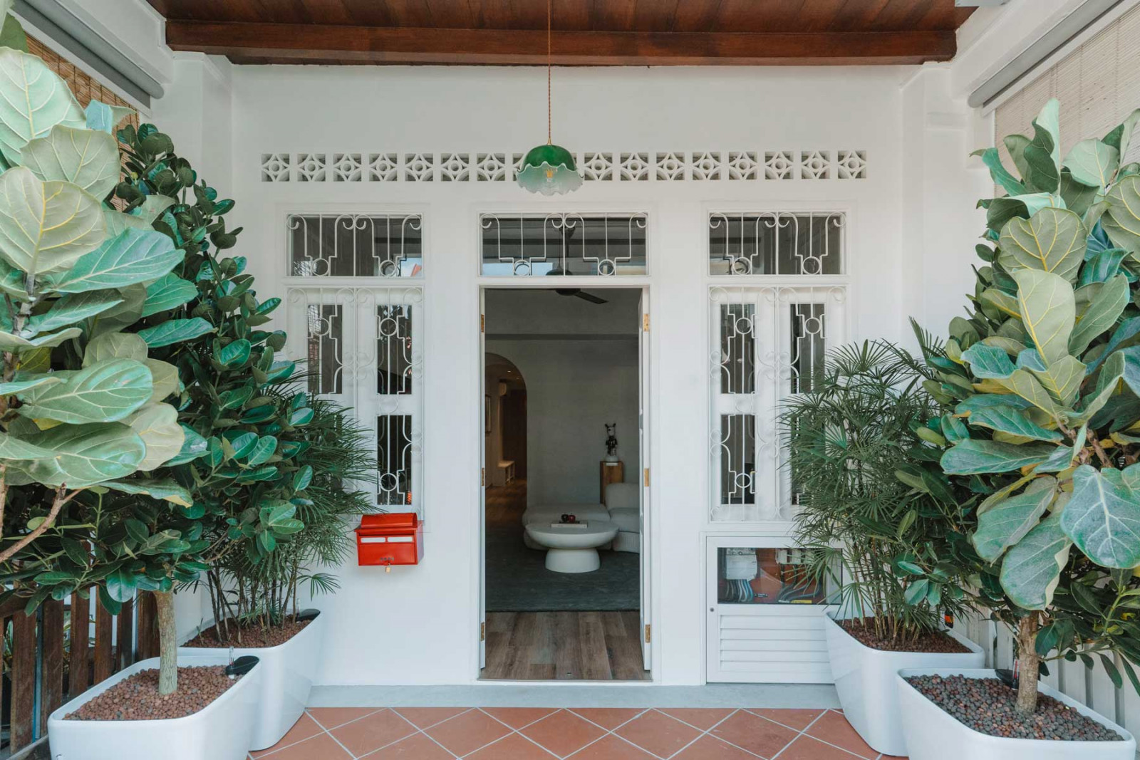 The entrance of the white-painted shophouse is framed by lush planters