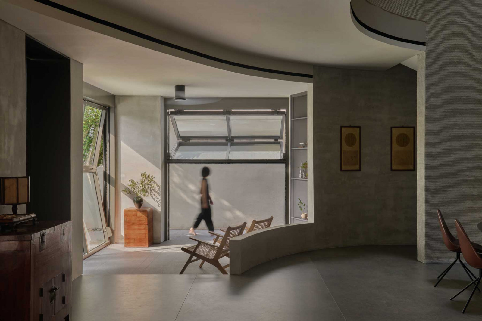 Glazed openings and a gentle curve in the concrete wall draw light and breeze into the living space, underscoring the passive design principles behind the 3D-printed home
