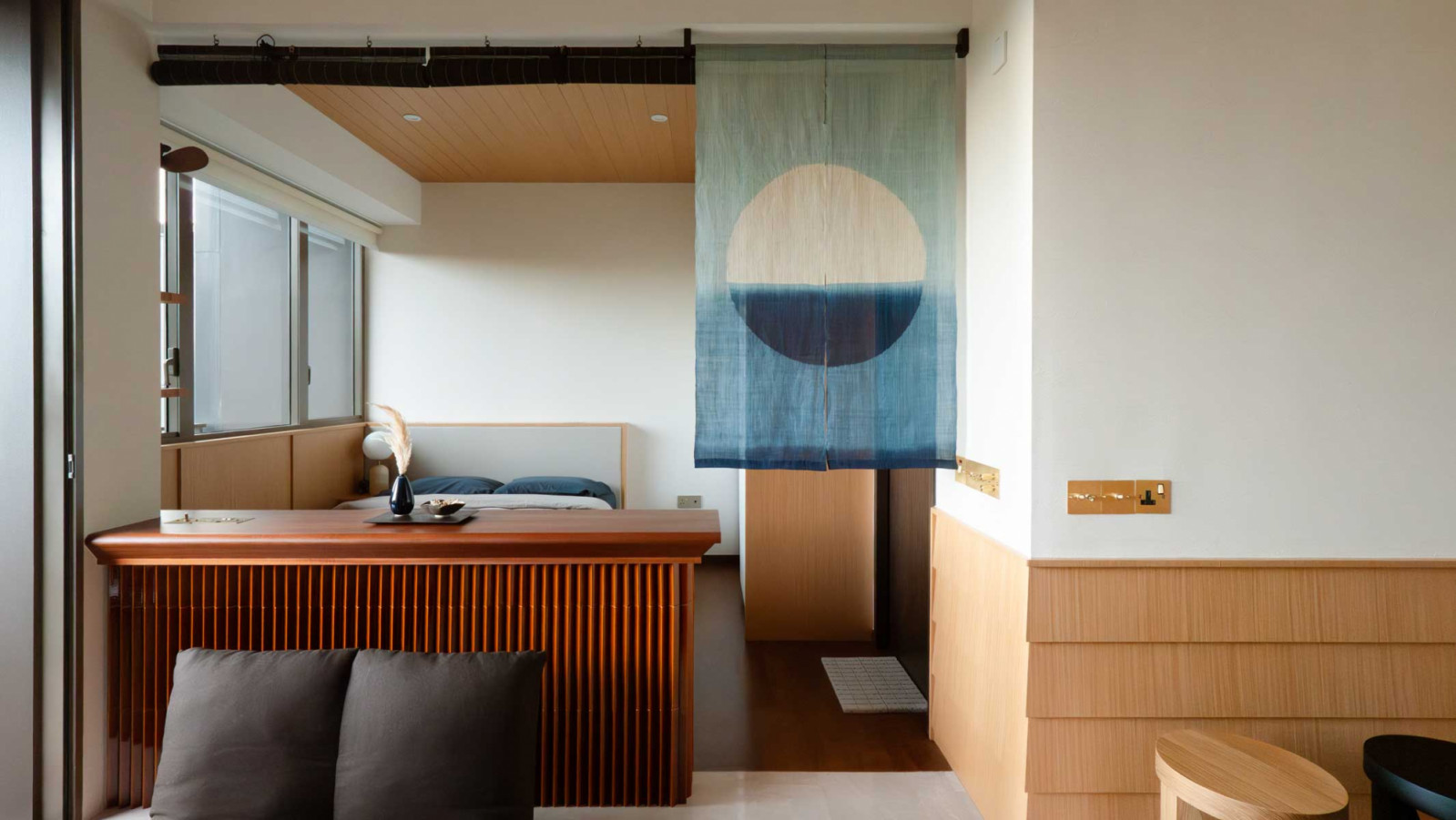 M.Interior reimagines the compact bedroom as a serene retreat, where a low-slung divider and timber-lined ceiling panels guide the eye forward—creating a sense of flow, calm, and quiet intention