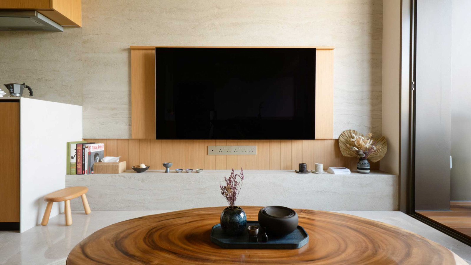 A monolithic stone and timber backdrop anchors the space, visually extending toward the balcony to amplify depth and openness