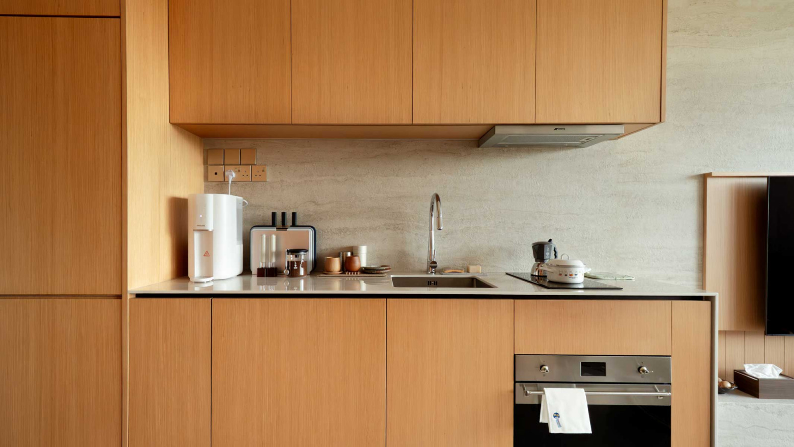 The compact kitchen is outfitted in light oak cabinetry and travertine-style stone, combining utility with seamless visual integration