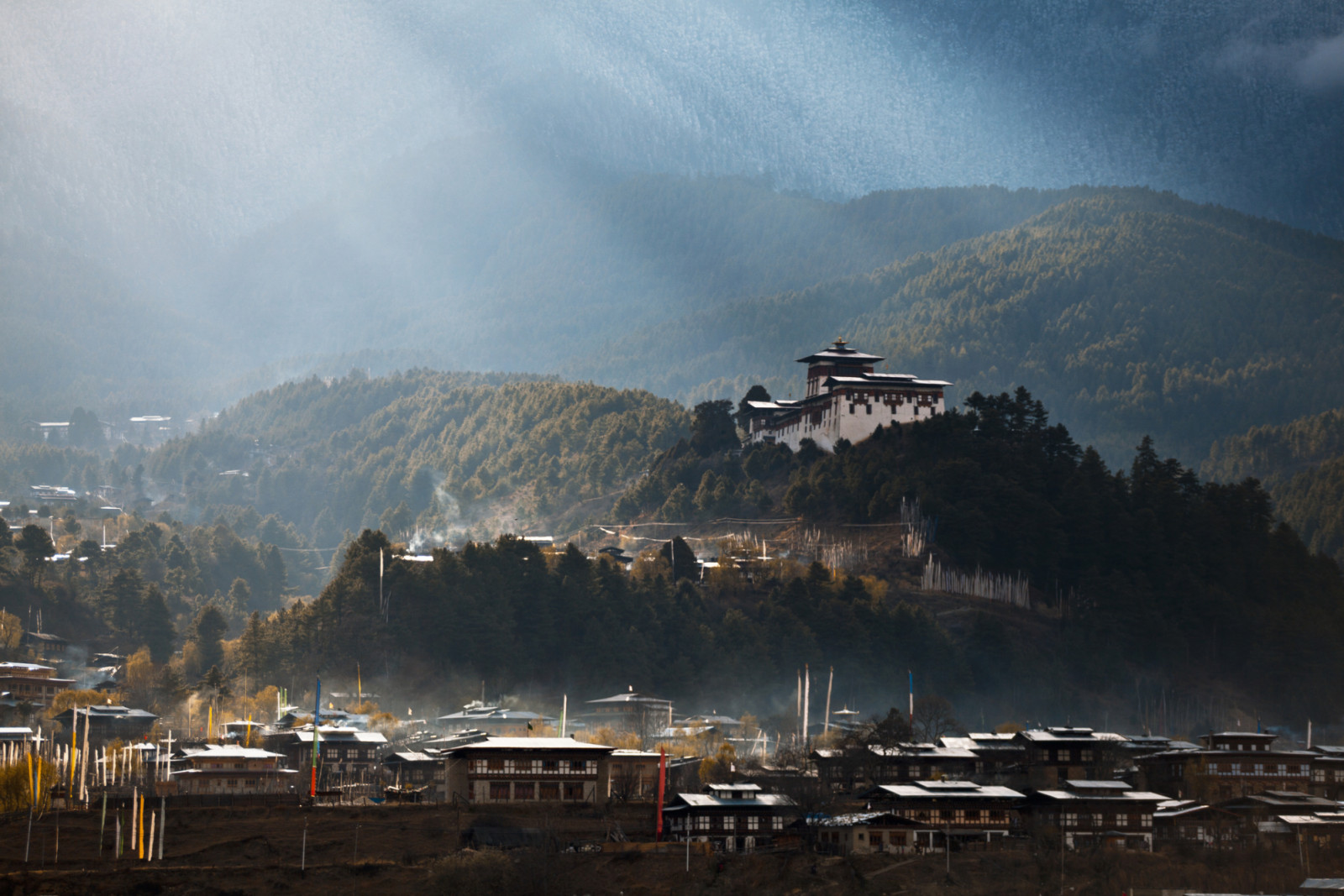 Morning sunrays over Jakar town and Dzong, fog rising from the town lit up.