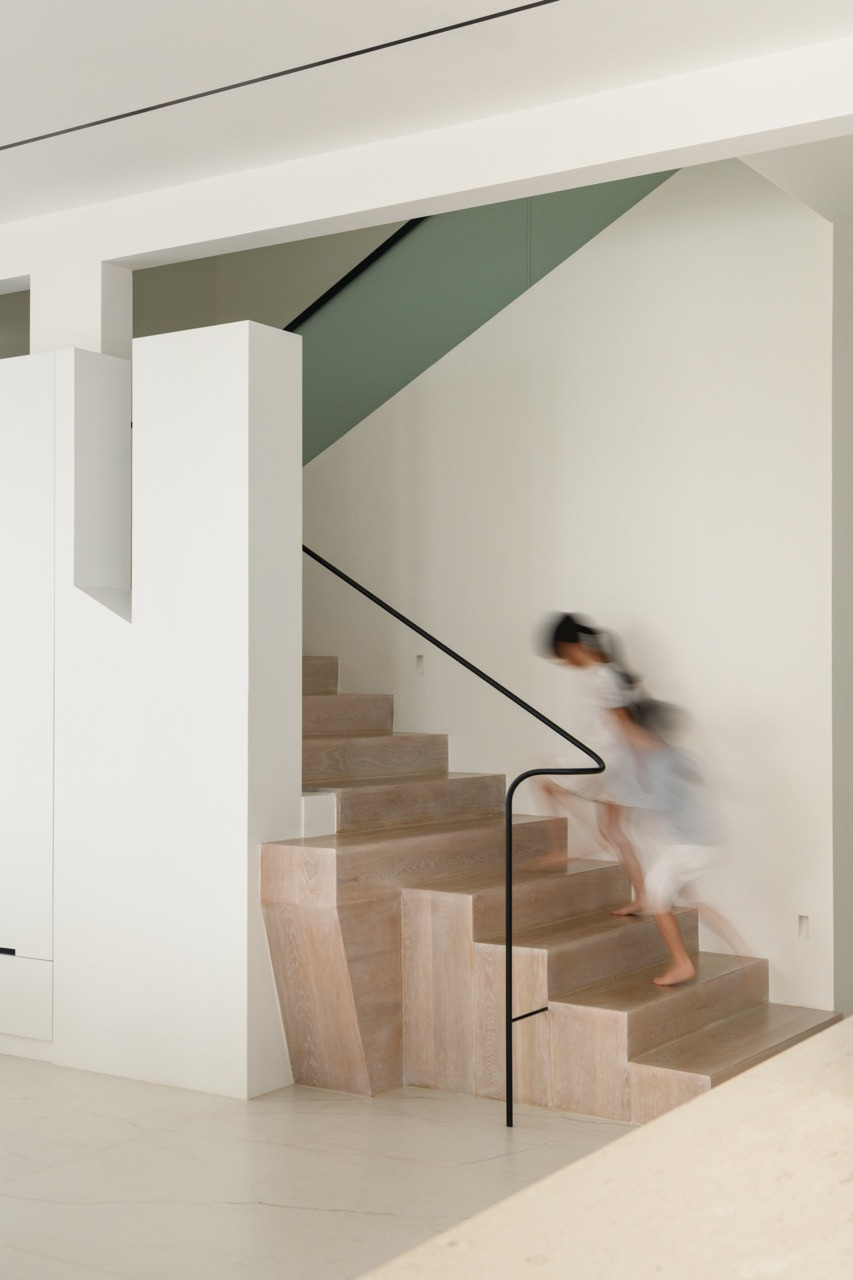 The interior staircase features the distinctive looping handrail bend referenced in the design, with timber treads adding warmth to the white composition