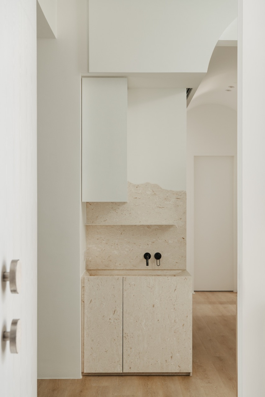 A powder room features a floating natural stone vanity with recessed storage
