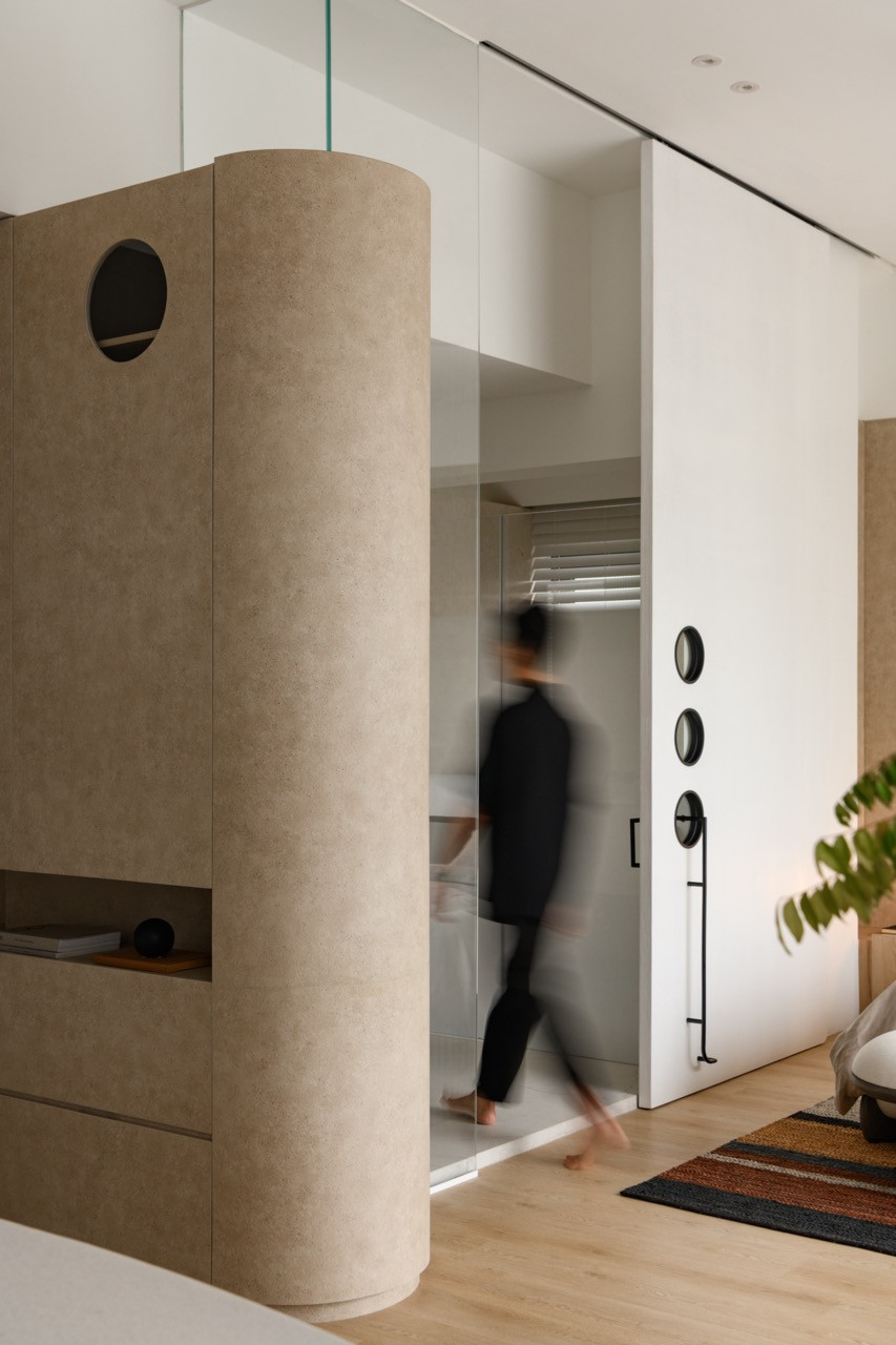 A curved natural stone pillar creates a sculptural moment in the master suite, with the sliding glass door system visible beyond