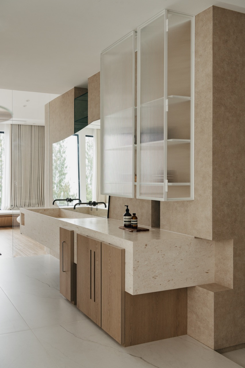 The bathroom vanity showcases natural stone and light timber accents, with fluted glass cabinetry adding textural interest