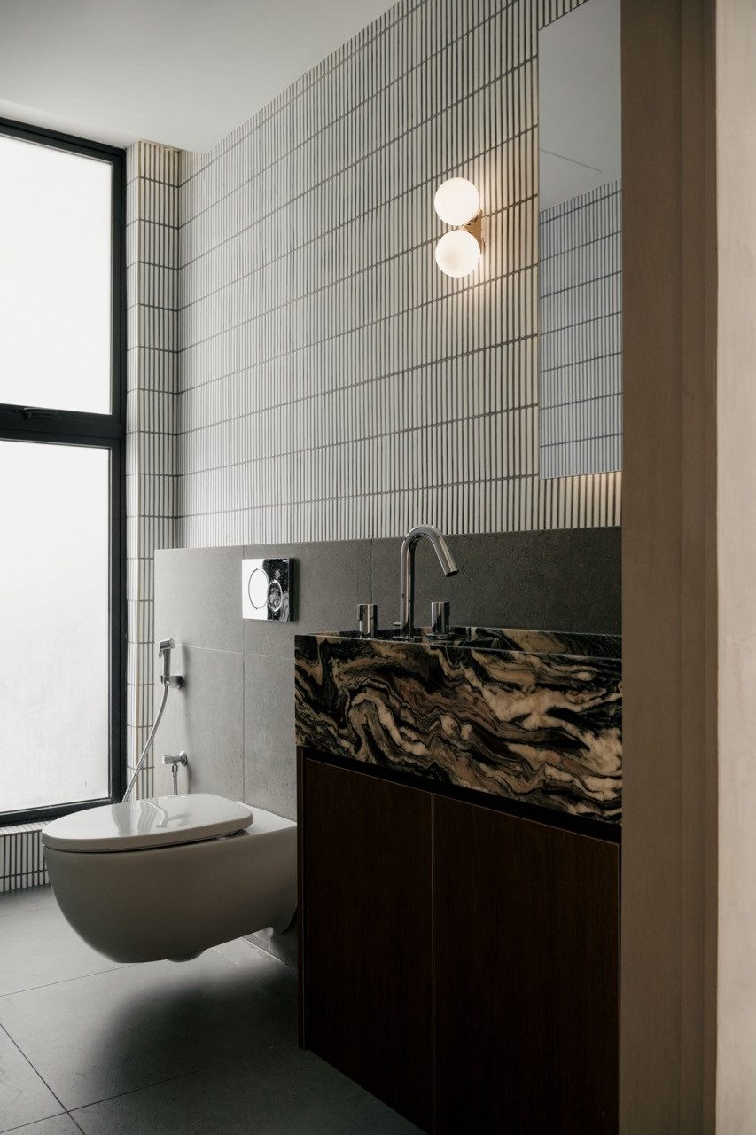 Textured tile walls and a dramatic marble vanity anchor the guest bathroom in the Petaling Jaya apartment