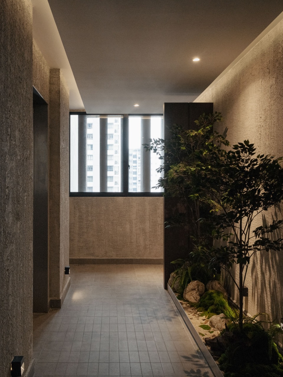 The shadowy entry garden features brushed cement walls and artificial plantings, creating deliberate darkness before the sun-filled living room
