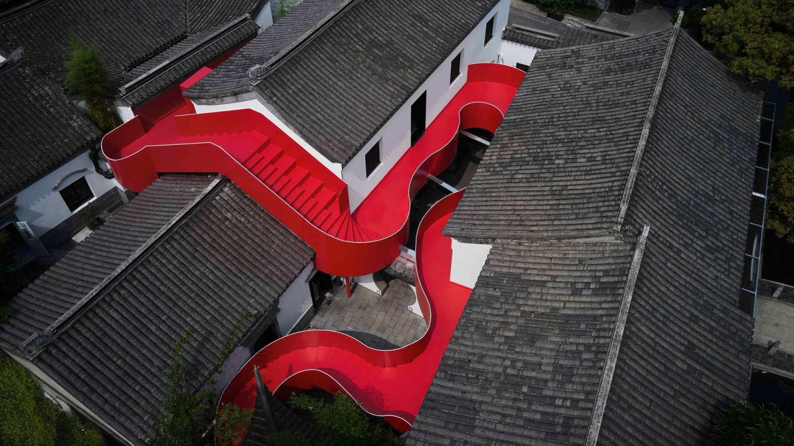 The serpentine red steel staircase commands attention with its vivid chroma and sculptural form