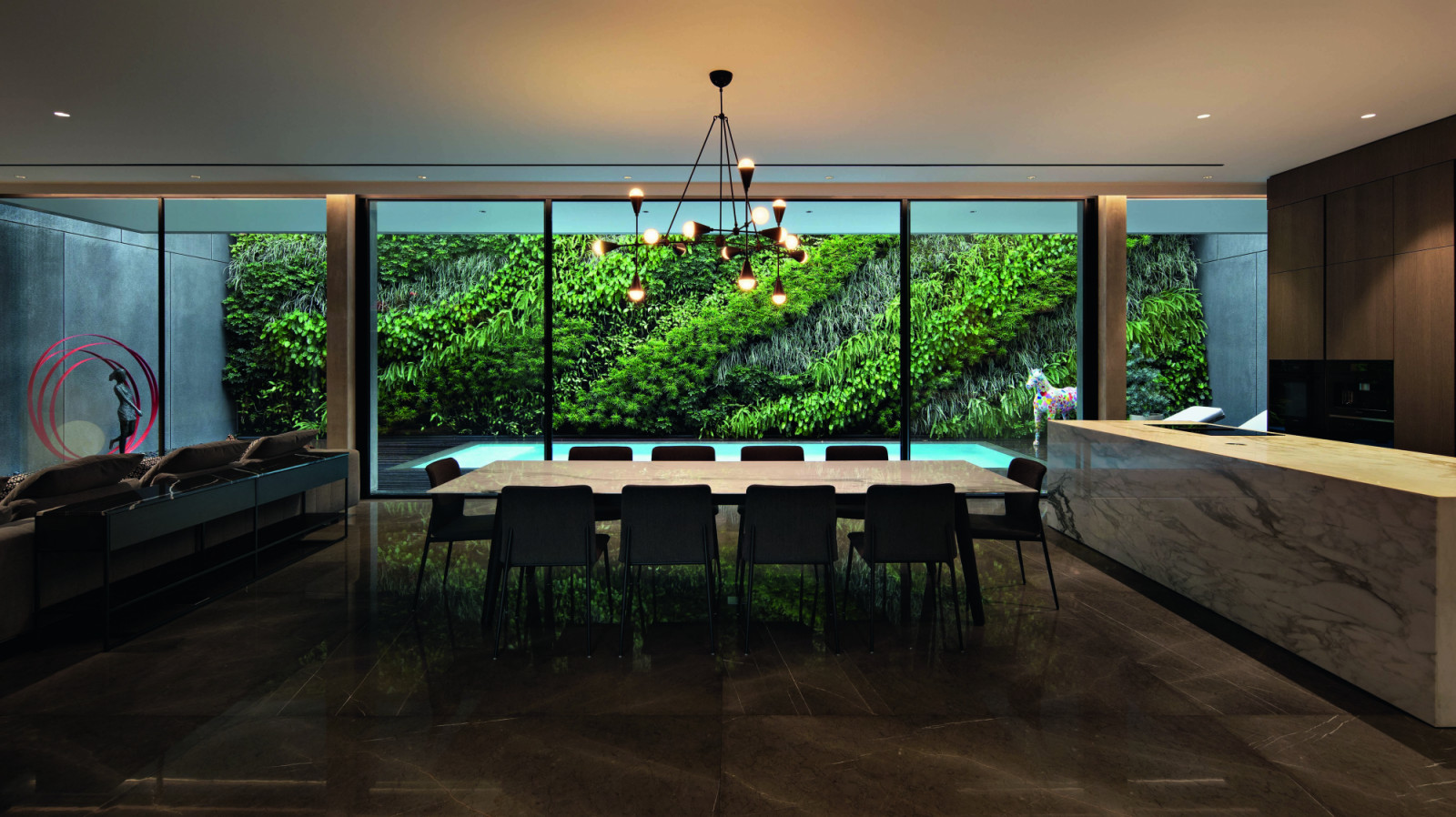 The living-dining area of the home overlooks the pool, with a lush vertical garden serving as a backdrop for a vibrant unicorn sculpture