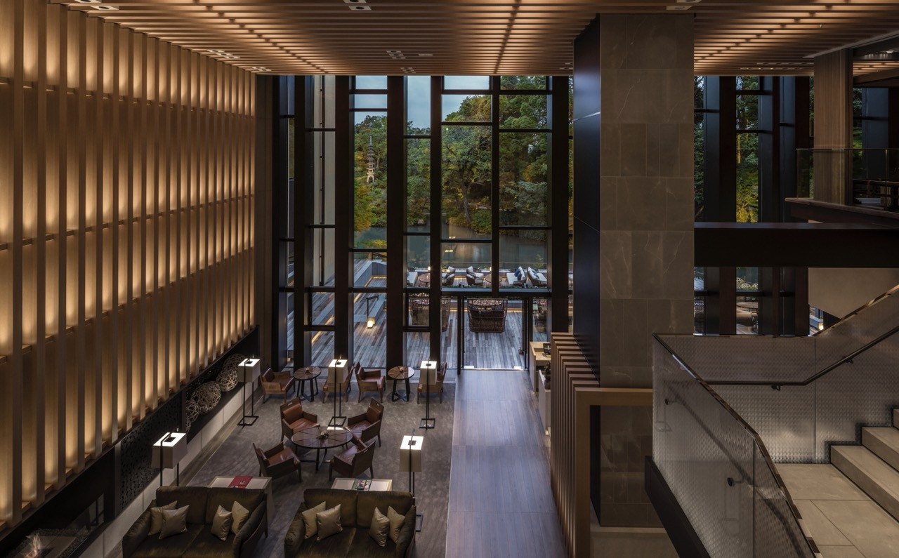 The double-height dining space incorporates illuminated wooden slat walls and opens directly to the pond garden through floor-to-ceiling glazing