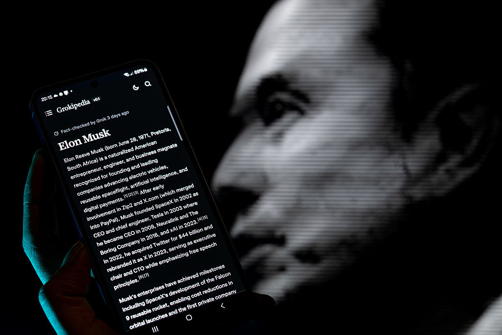 The Grokipedia application is displayed on a mobile phone with Elon Musk in the background, in this photo illustration in Brussels, Belgium, on October 30, 2025. (Photo by Jonathan Raa/NurPhoto via Getty Images)