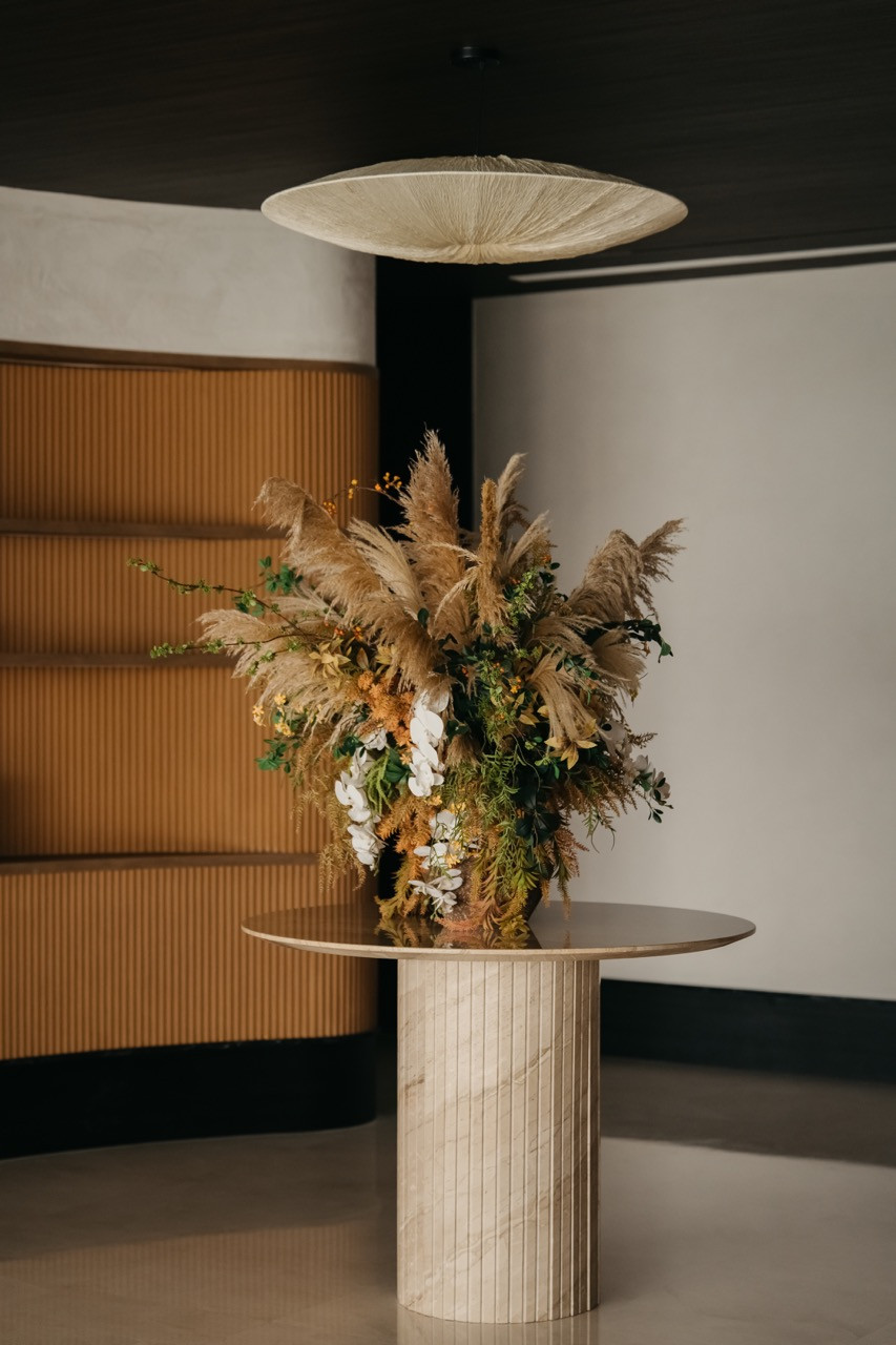 A fluted pendant light hangs above a cylindrical pedestal with a floral arrangement