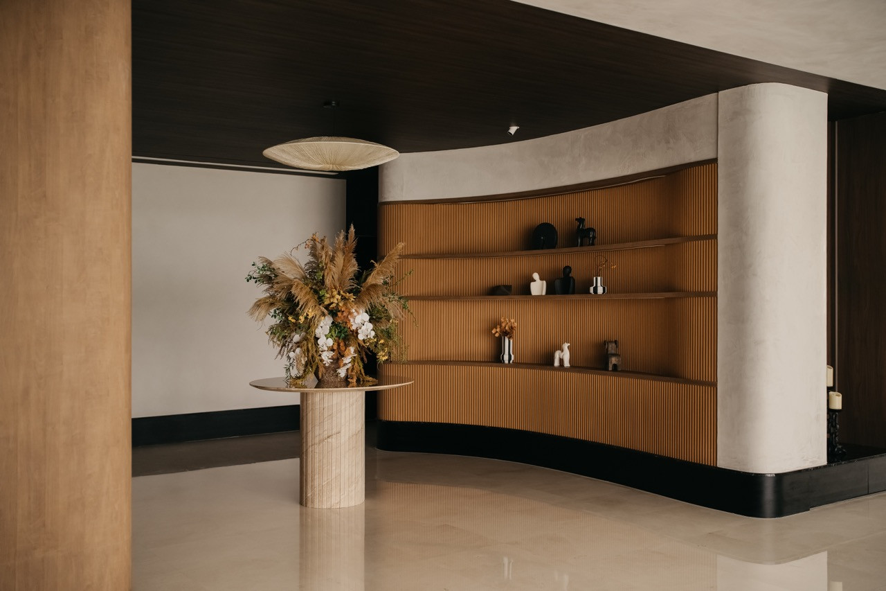 A curved display area features ribbed timber shelving and a cylindrical pedestal table contrasted with a dark ceiling