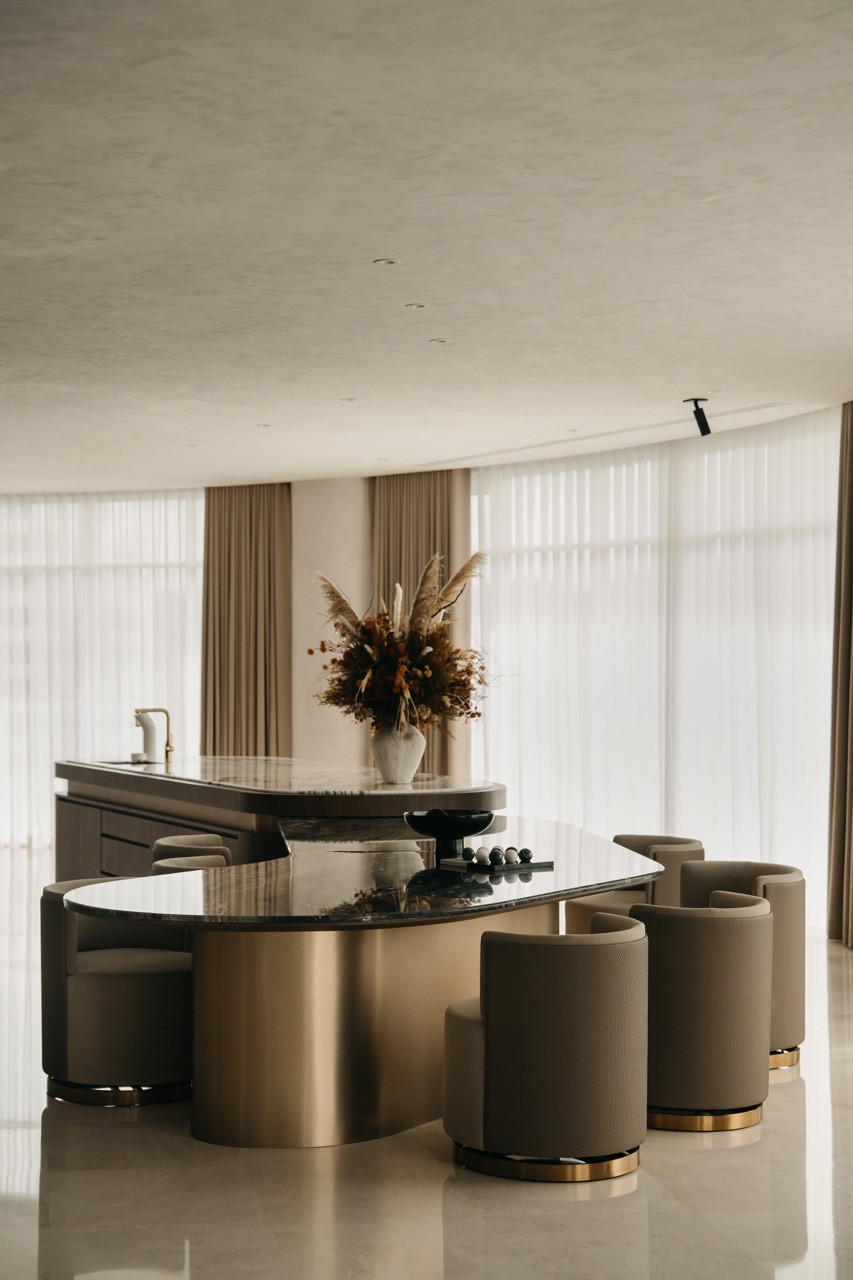 The curved island counter with a black marble top and brass base seats multiple diners