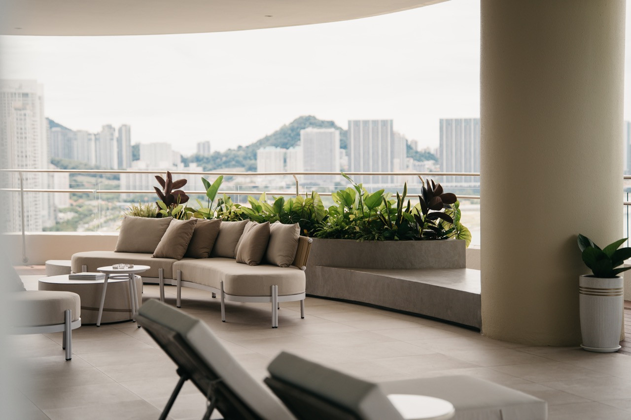 A seating area on the balcony includes a curved sofa and planters, and the balcony is at a high level, offering views across Penang.