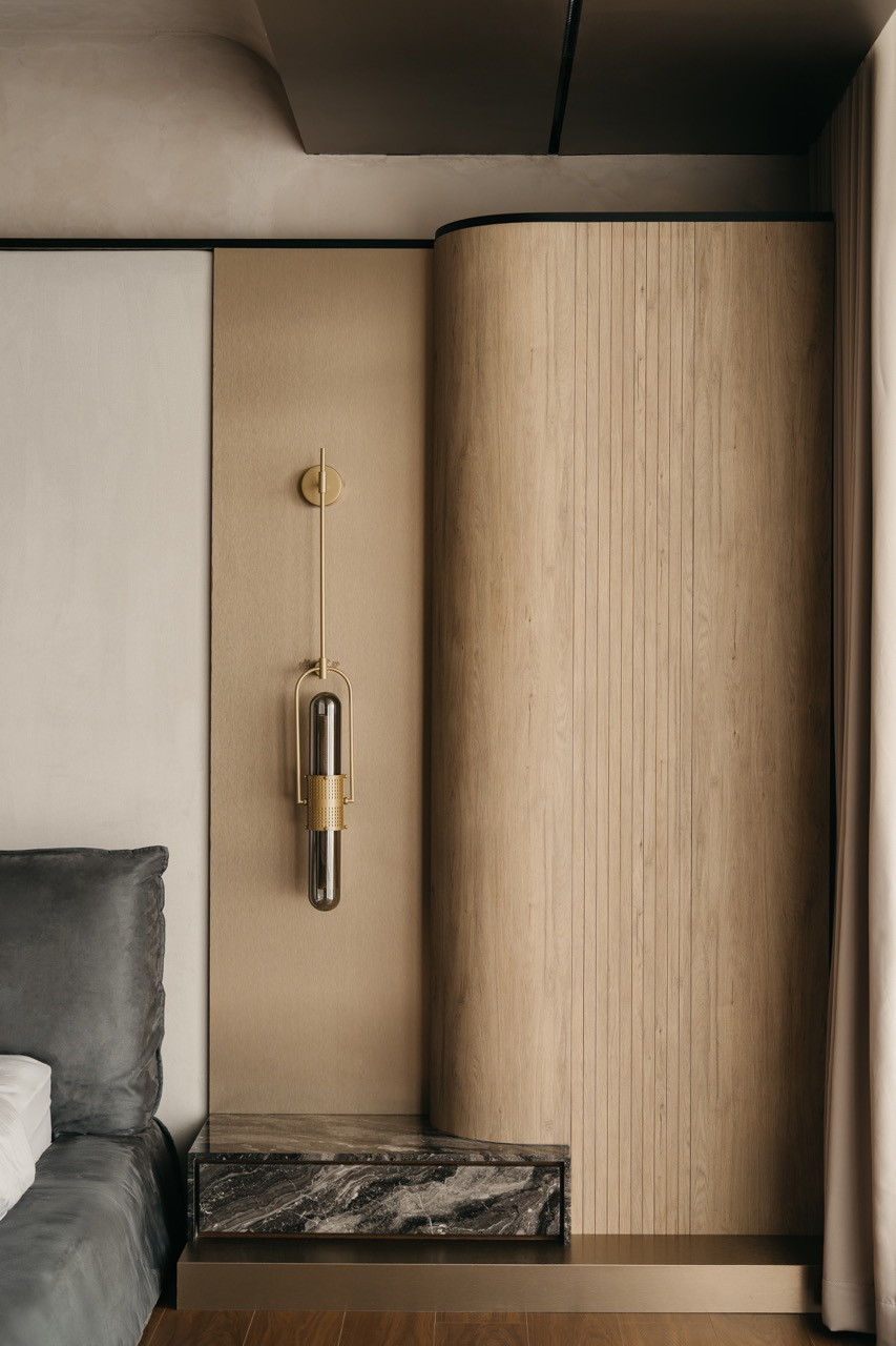 A bedroom wall detail shows a brass-and-glass sconce beside curved timber panelling with a marble shelf that sits below the light fixture