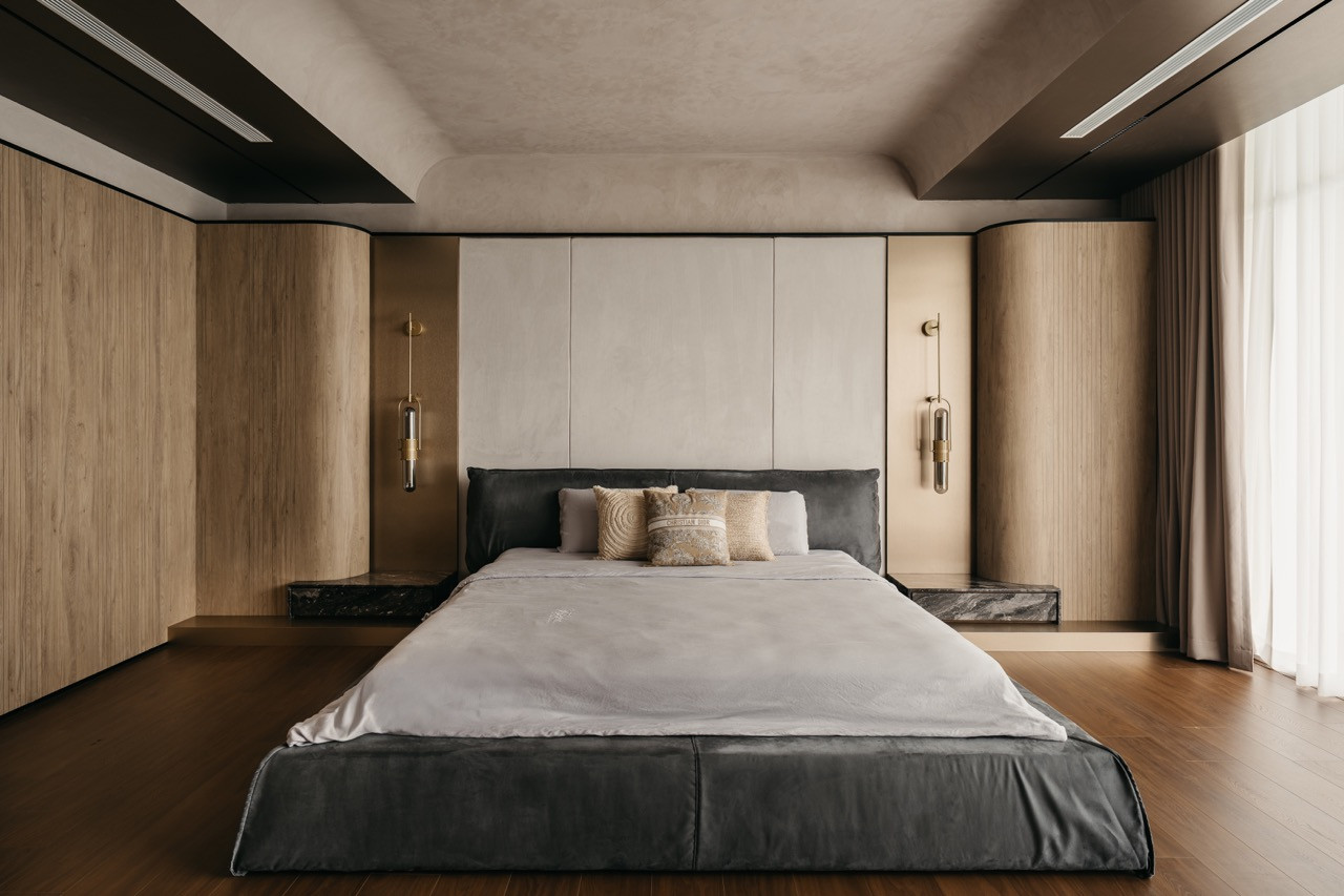 The master bedroom features a padded headboard, curved timber storage and brass wall sconces