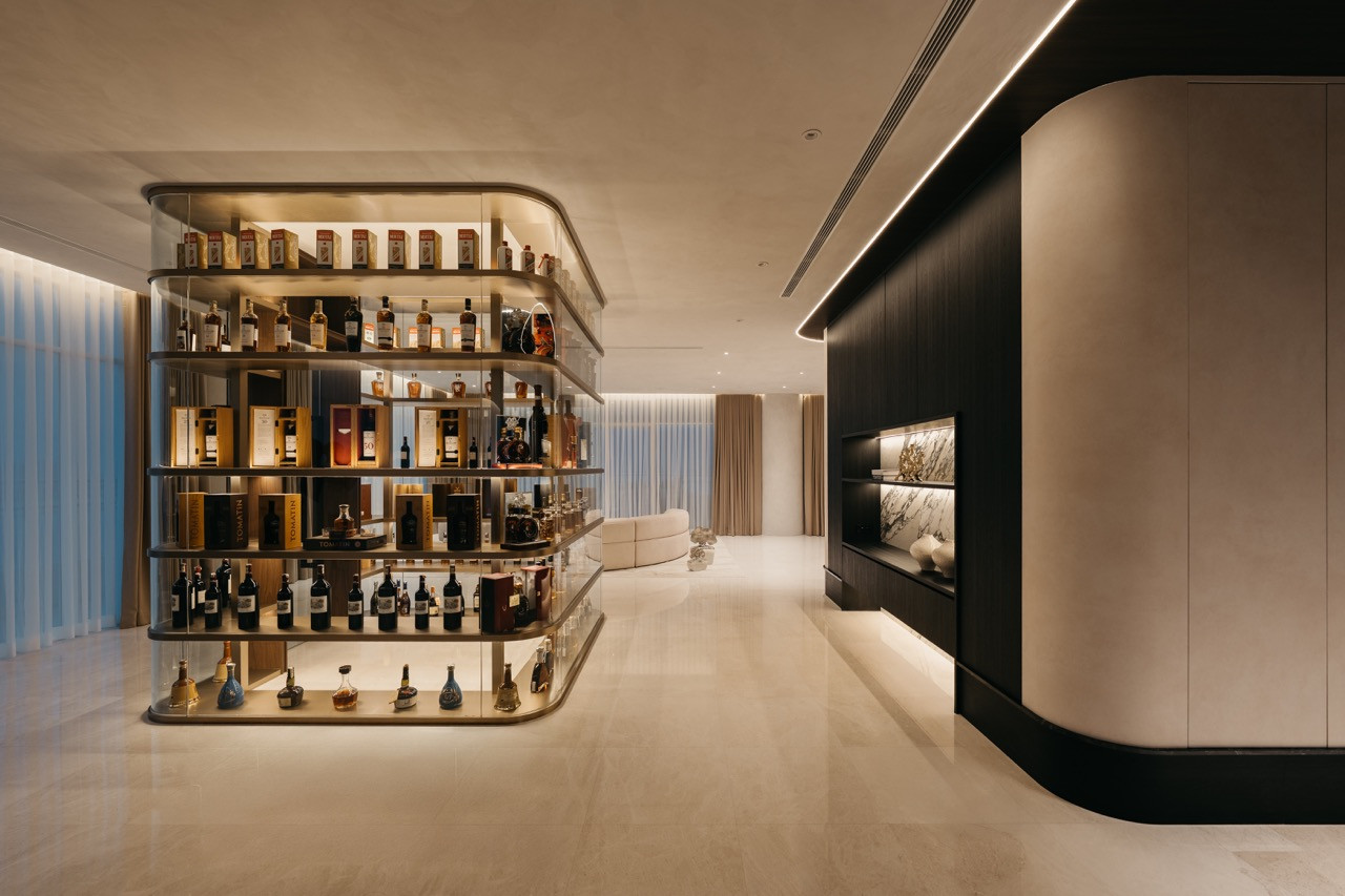 The curved spirits display cabinet stands near the living area. Floor-to-ceiling curtains line the exterior walls, which open to the balcony pool