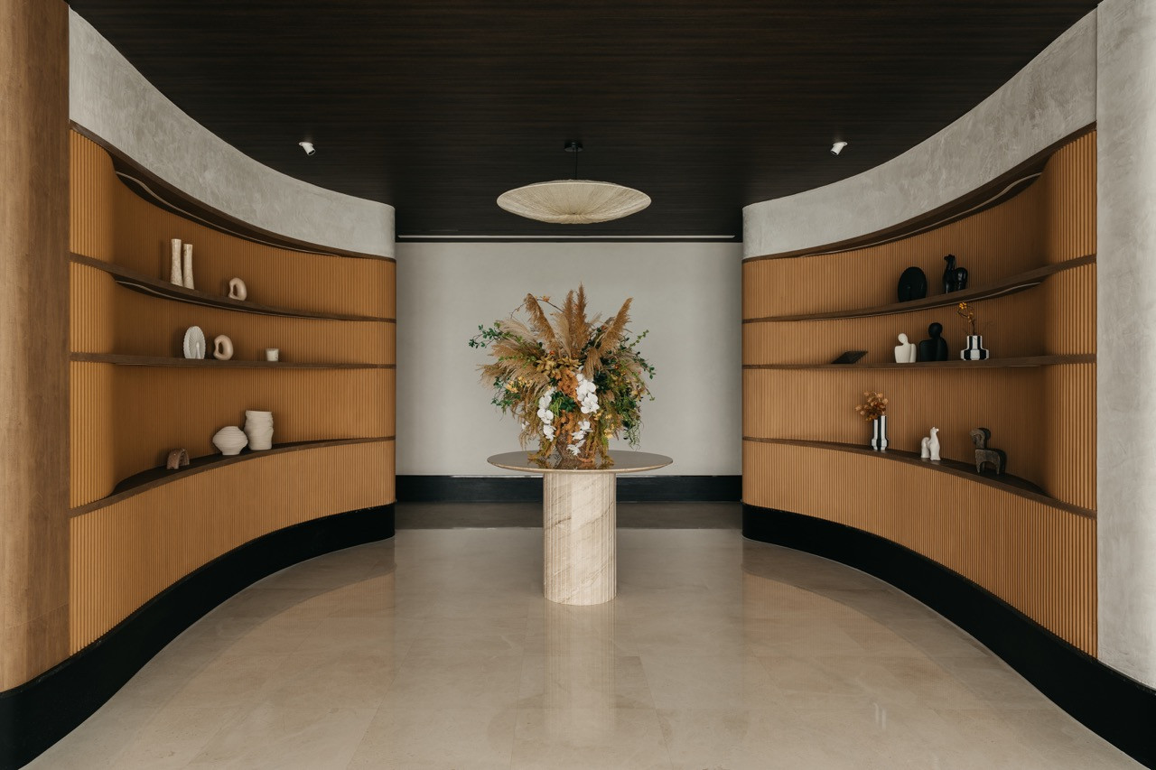 A symmetrical view of the curved display area shows matching shelving on both sides. The central pedestal table holds a floral arrangement beneath the pendant light