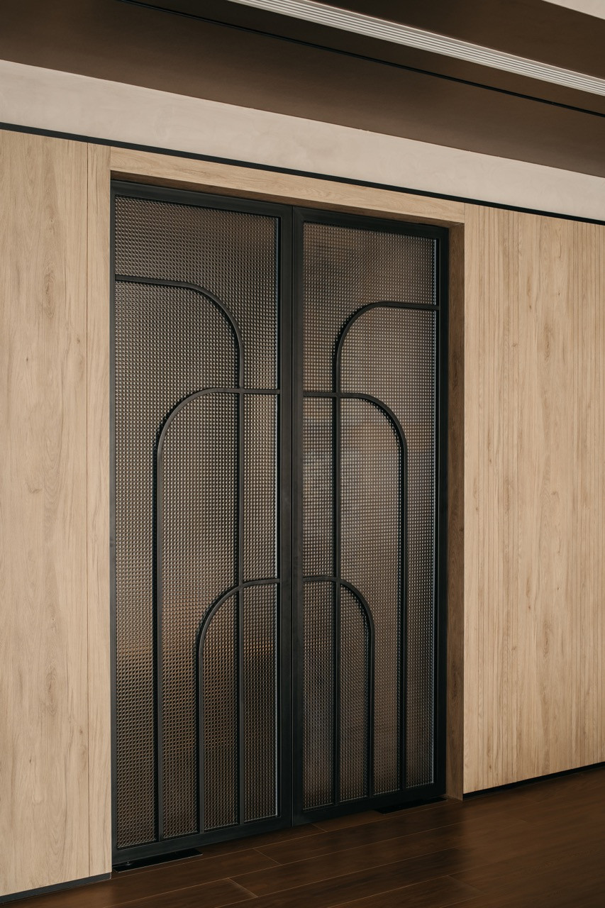 A decorative cabinet features black mesh panels with curved metal detailing set within timber cabinetry