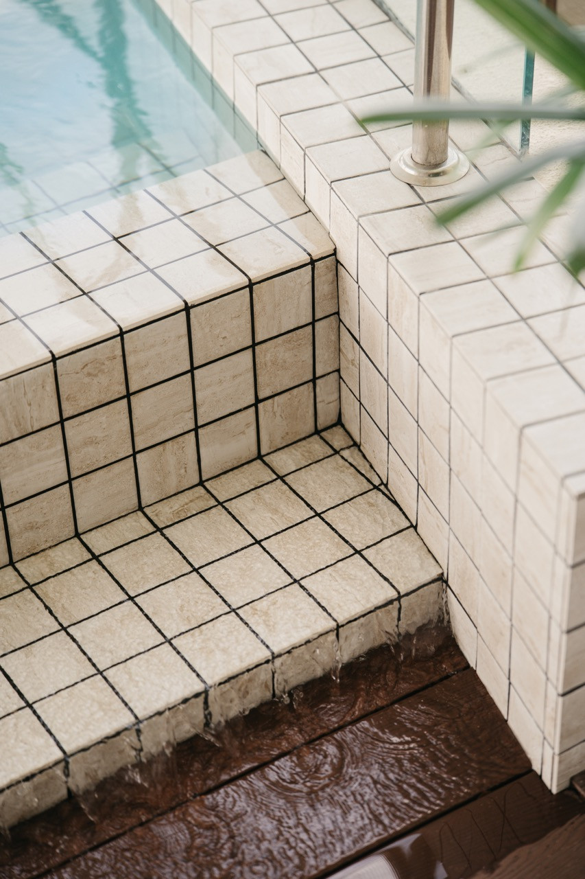 The balcony pool features tiled steps with a glass barrier, while the white mosaic tiles line the pool structure, which overlooks the cityscape
