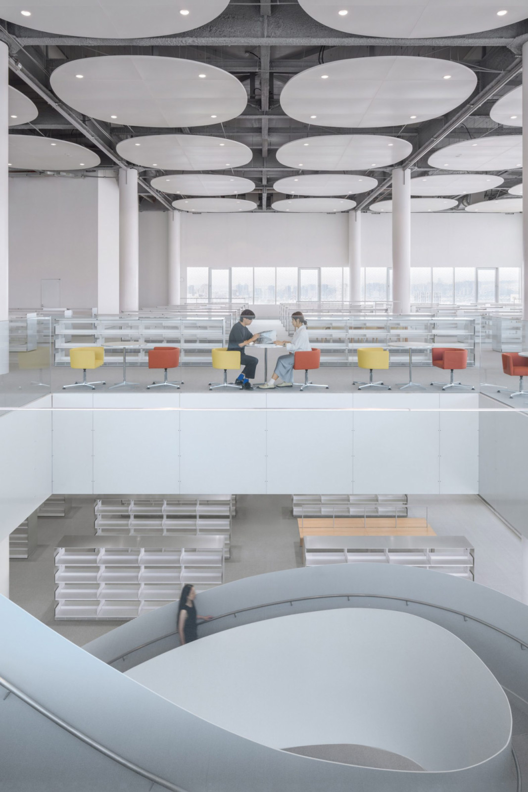 The library occupies one of three interconnected volumes, with low bookshelves arranged beneath circular acoustic ceiling panels (Photo: YHLAA)