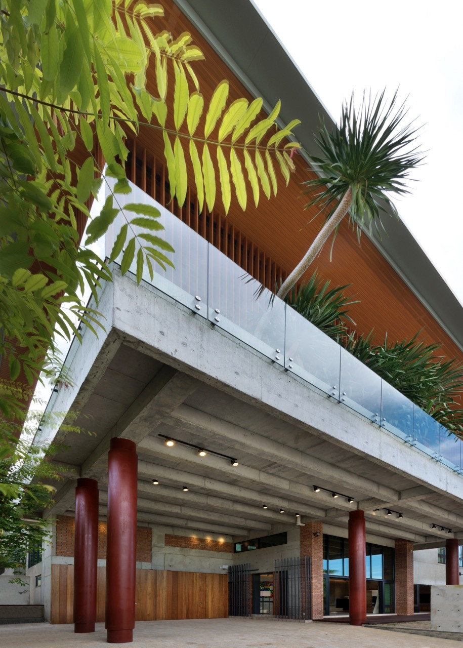 The sky garden also functions as a porte-cochère with large-diameter sienna red steel columns supporting the concrete structure above the covered entrance