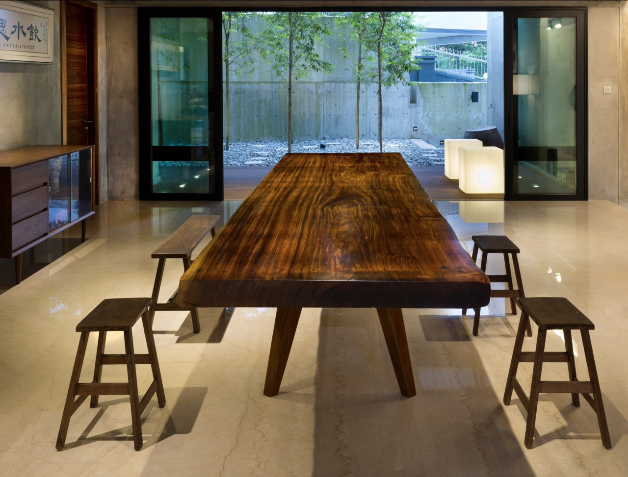 The dining table was crafted from a single timber slab, surrounded by simple wooden stools with full-height glazing framing views of the courtyard
