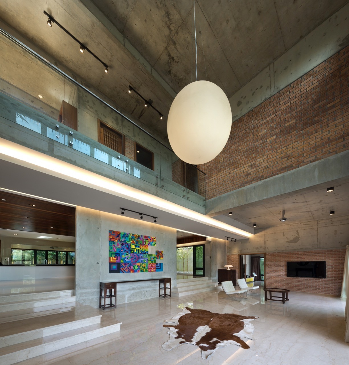 The living hall shows the double-volume space with exposed concrete structural beams and brick screen walls