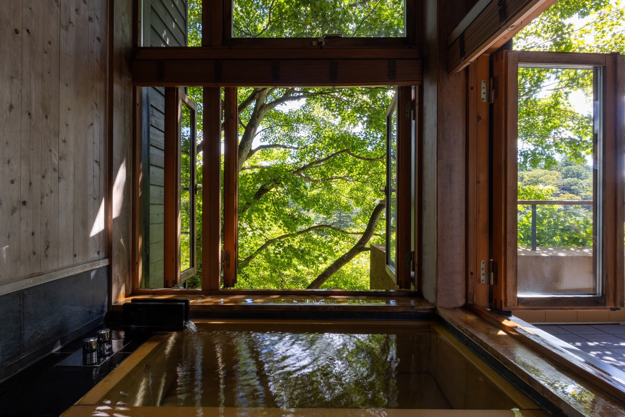 Windows in guest room baths frame the forest canopy, treating bathing as an activity oriented toward landscape observation rather than privacy
